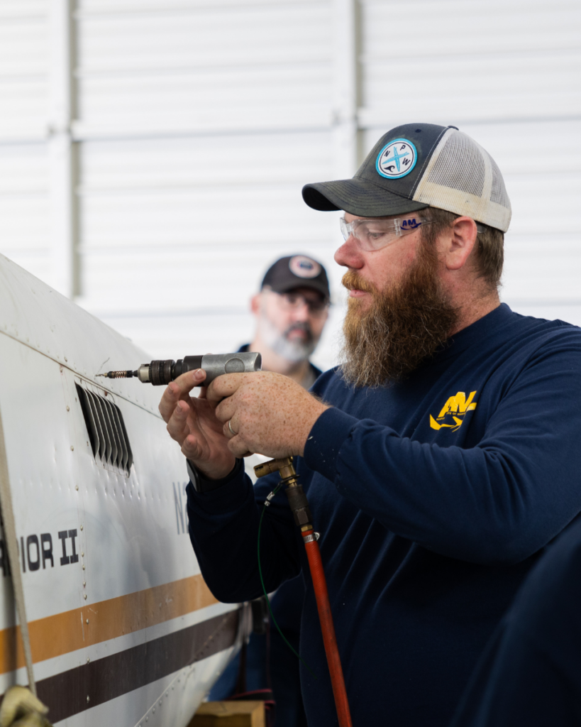 Aviation maintenance technician student at AIM using a pneumatic drill on an aircraft during hands-on training.